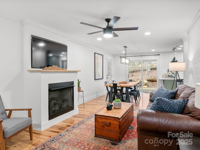 living area featuring baseboards, light wood-style flooring, recessed lighting, a fireplace, and ornamental molding