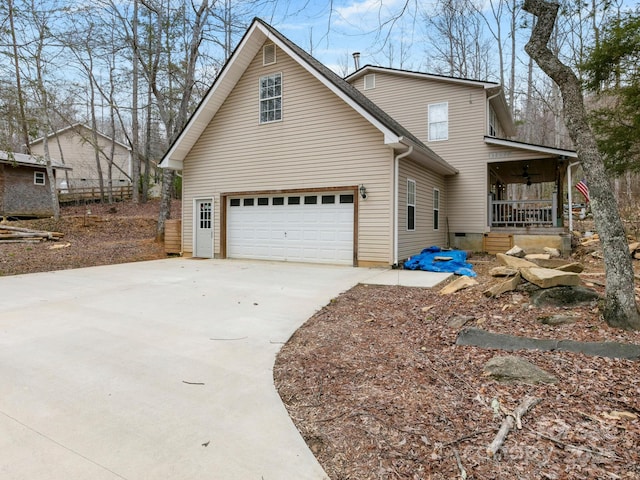 view of side of home featuring a garage, covered porch, concrete driveway, and a ceiling fan