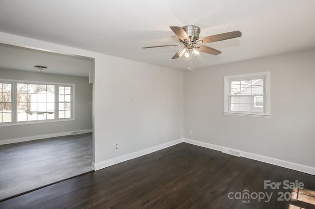 empty room with a wealth of natural light, dark wood finished floors, baseboards, and ceiling fan