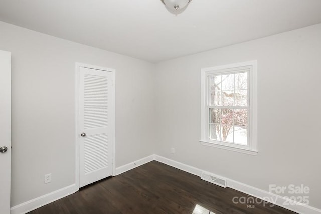 unfurnished bedroom with dark wood finished floors, visible vents, a closet, and baseboards