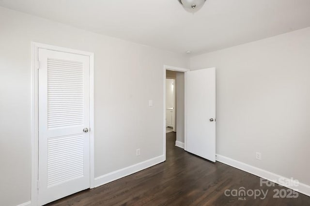 unfurnished bedroom with dark wood finished floors, a closet, and baseboards