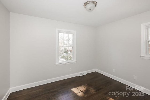 unfurnished room featuring dark wood-style floors, visible vents, and baseboards