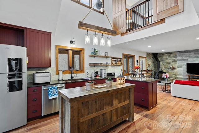 kitchen with a sink, open shelves, a kitchen island, appliances with stainless steel finishes, and a wood stove