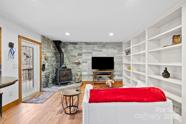 living area featuring built in features, recessed lighting, wood-type flooring, baseboards, and a wood stove