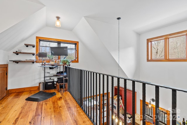 corridor with baseboards, light wood-style flooring, and vaulted ceiling