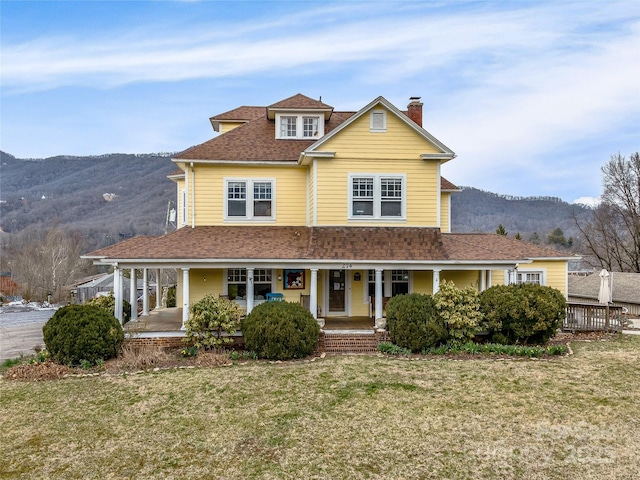 view of front of property with a front yard, covered porch, a chimney, a shingled roof, and a mountain view