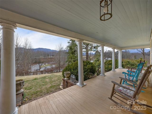 wooden deck with covered porch, a lawn, and a mountain view