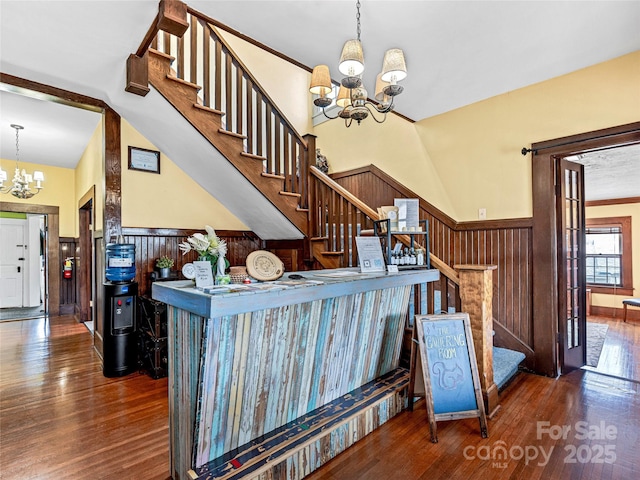 stairs with wooden walls, a notable chandelier, wood finished floors, and wainscoting