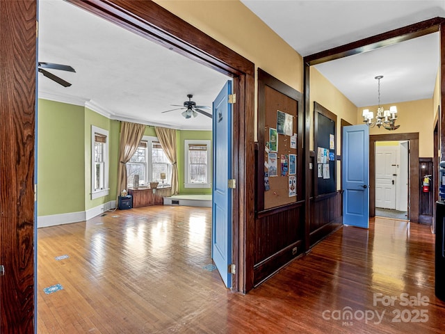 hall featuring a notable chandelier, wood finished floors, baseboards, and ornamental molding