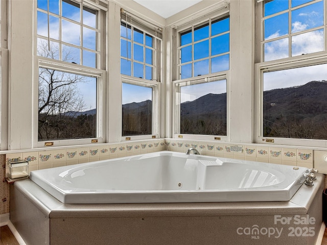 bathroom featuring a wealth of natural light, a tub with jets, and a mountain view