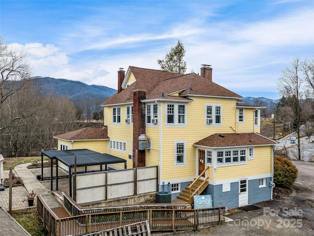 back of property featuring a deck with mountain view, central AC, stairway, a shingled roof, and a chimney