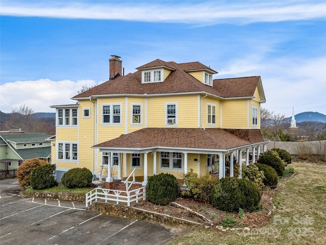 view of front of property with uncovered parking, covered porch, roof with shingles, and a chimney