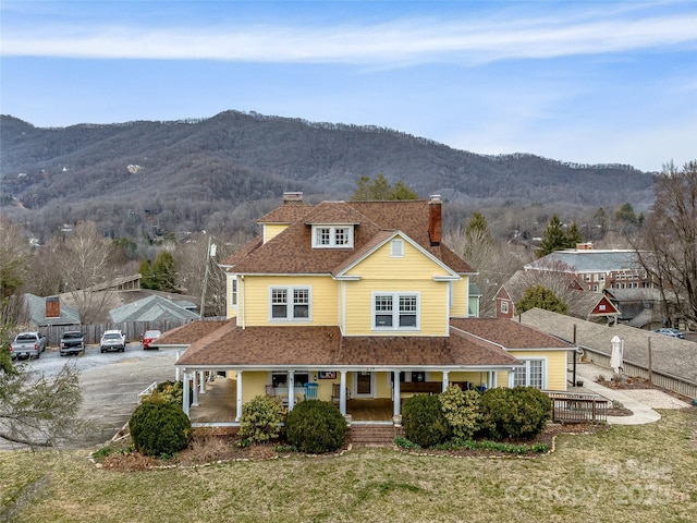 view of front of house with fence, a mountain view, roof with shingles, covered porch, and a chimney