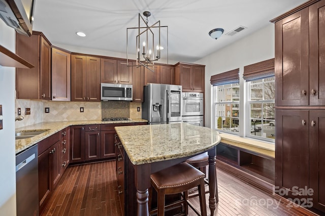 kitchen with visible vents, dark wood-style flooring, decorative backsplash, appliances with stainless steel finishes, and a kitchen breakfast bar