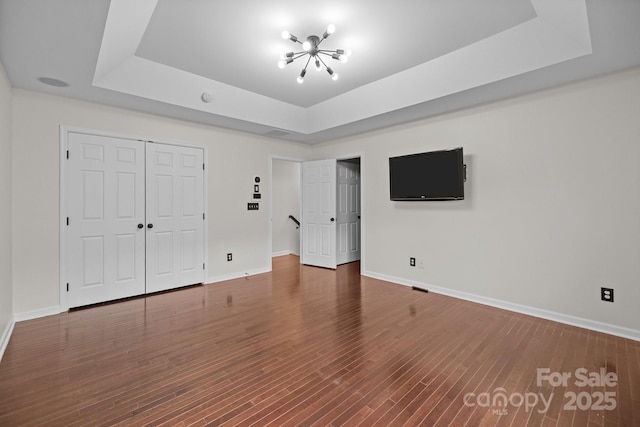 unfurnished bedroom with baseboards, a tray ceiling, wood finished floors, a closet, and a notable chandelier