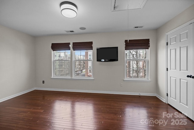 unfurnished room with hardwood / wood-style floors, attic access, baseboards, and visible vents