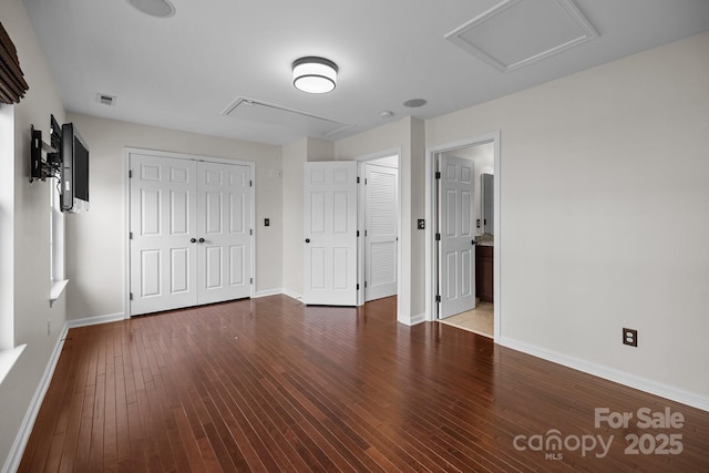 unfurnished bedroom featuring hardwood / wood-style floors, visible vents, baseboards, attic access, and a closet