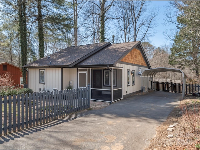 rustic home with aphalt driveway, a shingled roof, fence, a detached carport, and a sunroom