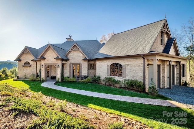 french country style house with a garage, a chimney, a front lawn, and a shingled roof