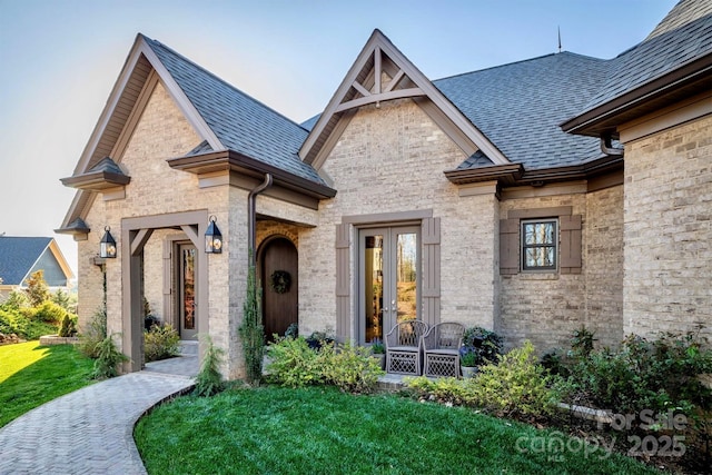 view of front of house featuring brick siding, french doors, and roof with shingles