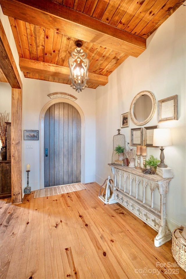 entrance foyer with beamed ceiling, hardwood / wood-style flooring, arched walkways, an inviting chandelier, and wood ceiling