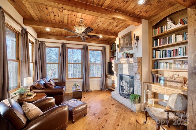 living area featuring built in features, a stone fireplace, wood ceiling, light wood-style floors, and beamed ceiling