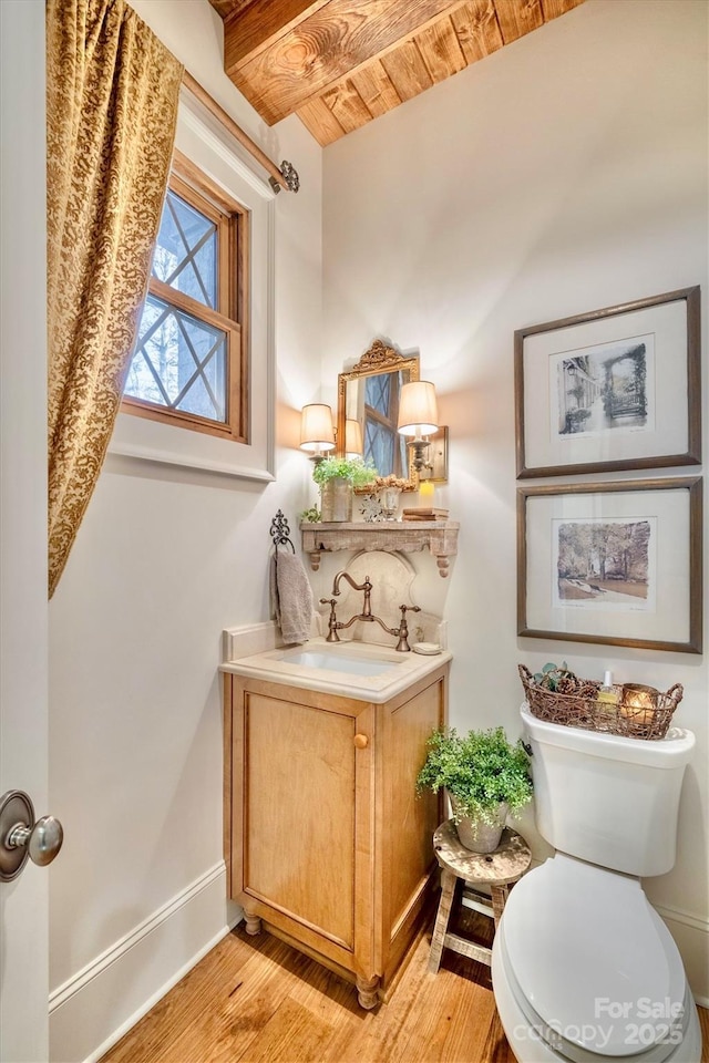 half bath featuring toilet, wood finished floors, baseboards, wood ceiling, and vanity