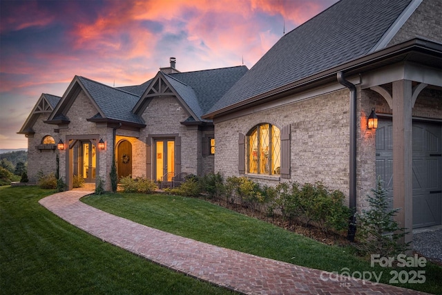 french country inspired facade featuring a lawn, a chimney, french doors, and a shingled roof