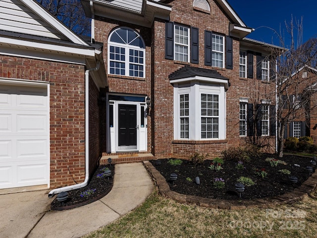 view of exterior entry featuring an attached garage and brick siding