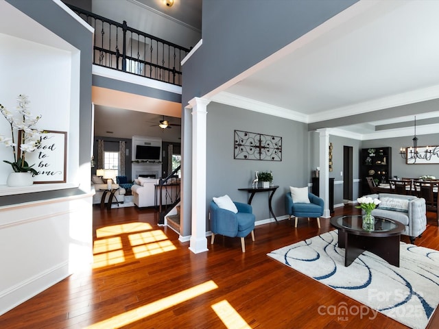 living room with baseboards, ornate columns, a fireplace, wood-type flooring, and ceiling fan with notable chandelier