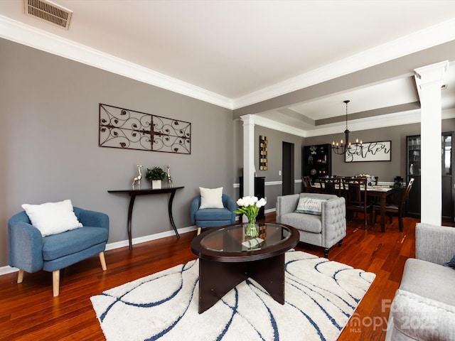 living area featuring visible vents, a chandelier, ornamental molding, decorative columns, and wood finished floors