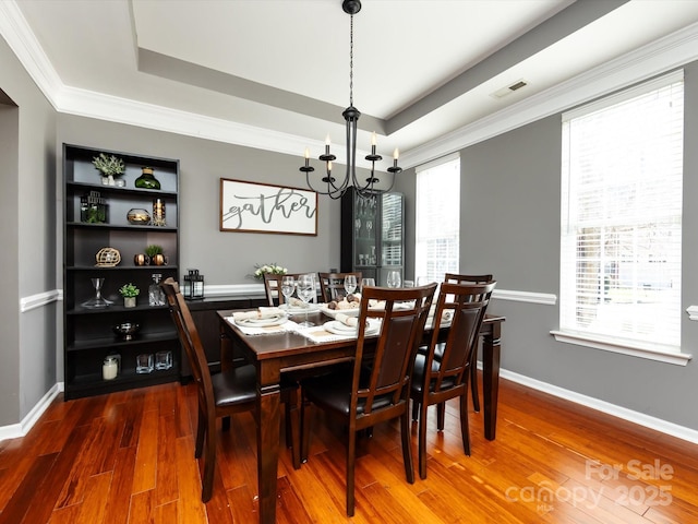 dining area featuring a tray ceiling, baseboards, visible vents, and wood finished floors