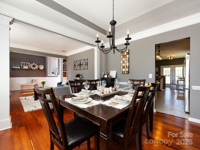 dining space featuring dark wood-type flooring, a wainscoted wall, ornate columns, and a chandelier