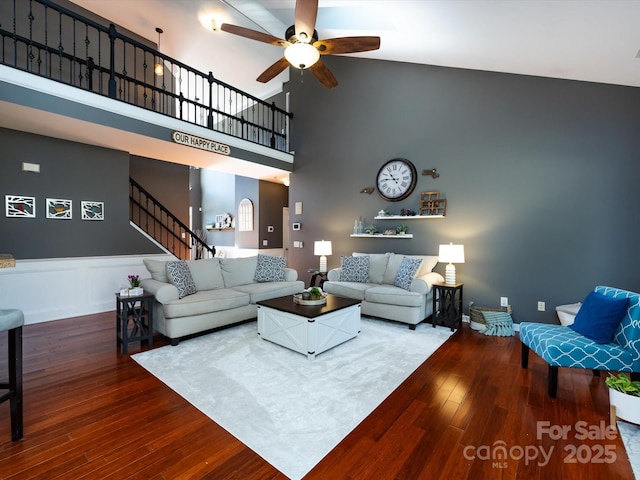 living area with hardwood / wood-style floors, a ceiling fan, high vaulted ceiling, stairs, and wainscoting