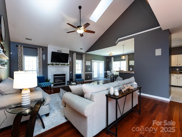 living area with baseboards, a fireplace, a skylight, wood finished floors, and a ceiling fan