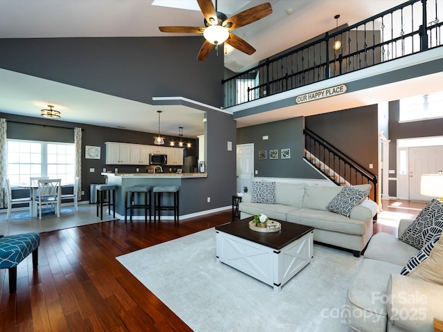 living room with high vaulted ceiling, a ceiling fan, wood finished floors, stairway, and baseboards