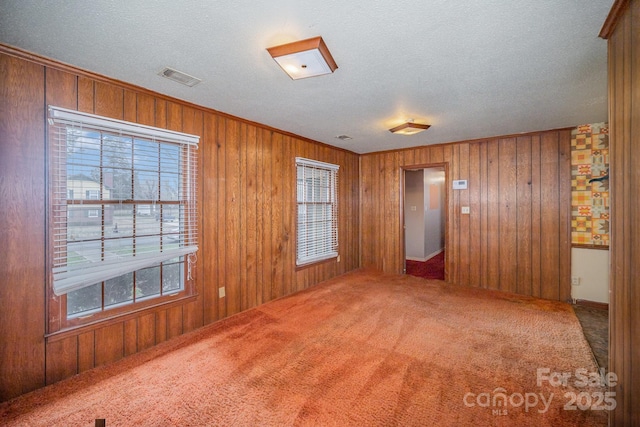 carpeted spare room featuring wooden walls, visible vents, and a textured ceiling