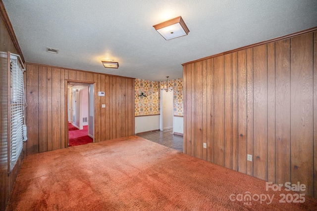 carpeted empty room featuring wooden walls, visible vents, and a textured ceiling