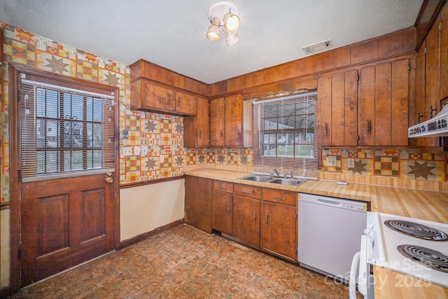 kitchen featuring brown cabinets, a sink, under cabinet range hood, white appliances, and baseboards