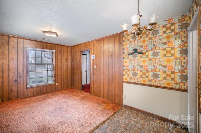 carpeted spare room with visible vents, a notable chandelier, a textured ceiling, wooden walls, and crown molding