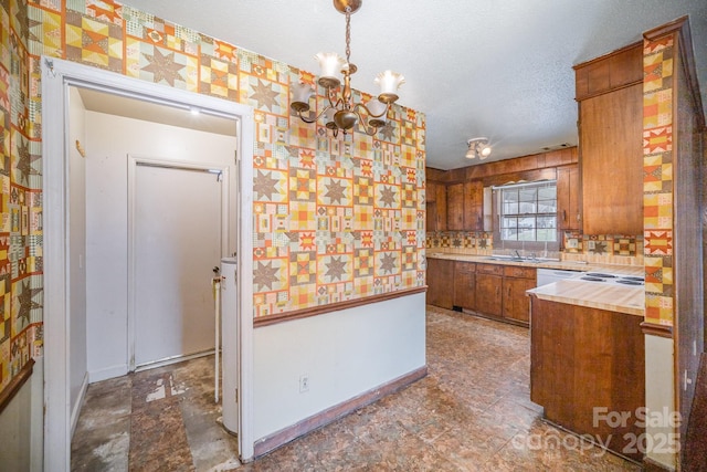 kitchen featuring a sink, wallpapered walls, a textured ceiling, brown cabinetry, and light countertops