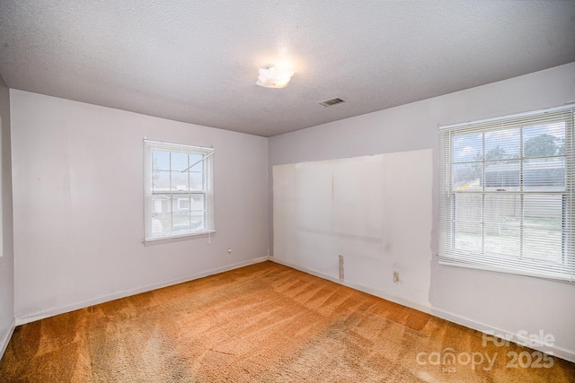 empty room featuring light carpet, visible vents, a textured ceiling, and baseboards