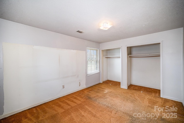 unfurnished bedroom with visible vents, two closets, a textured ceiling, carpet flooring, and baseboards