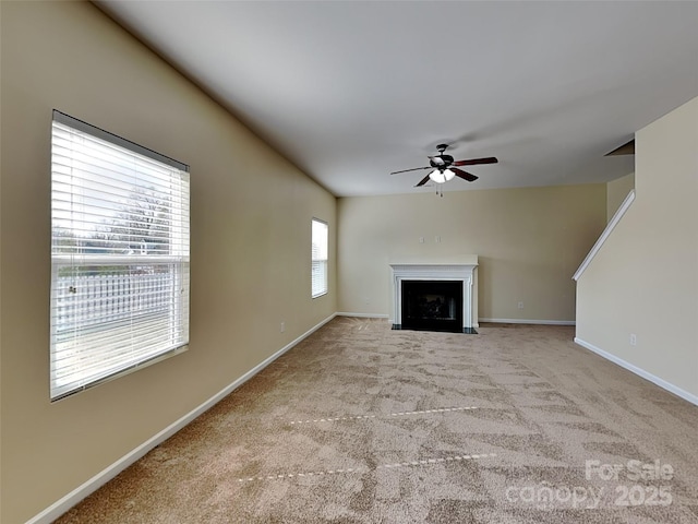 unfurnished living room featuring baseboards, a fireplace with flush hearth, carpet floors, and ceiling fan