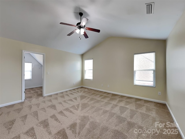 empty room featuring a wealth of natural light, visible vents, light colored carpet, and vaulted ceiling