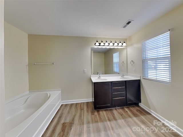 bathroom with visible vents, a garden tub, double vanity, wood finished floors, and a sink