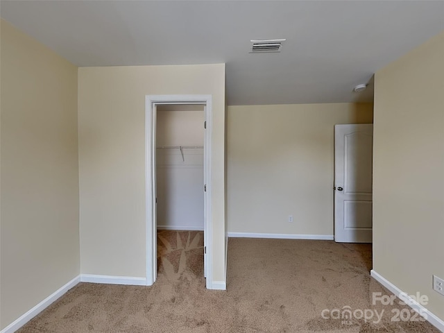 unfurnished bedroom featuring visible vents, baseboards, a walk in closet, and carpet