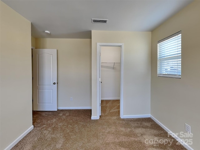 unfurnished bedroom with visible vents, a walk in closet, a closet, carpet, and baseboards