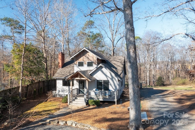 view of front facade featuring gravel driveway, fence, and a chimney