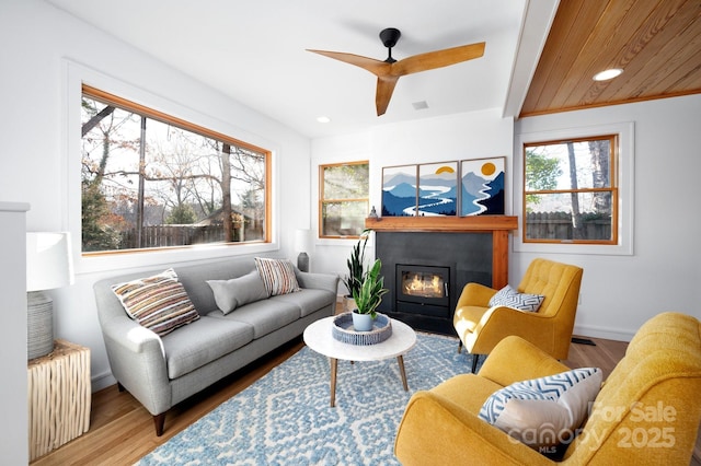 living room featuring visible vents, baseboards, ceiling fan, a fireplace with flush hearth, and wood finished floors